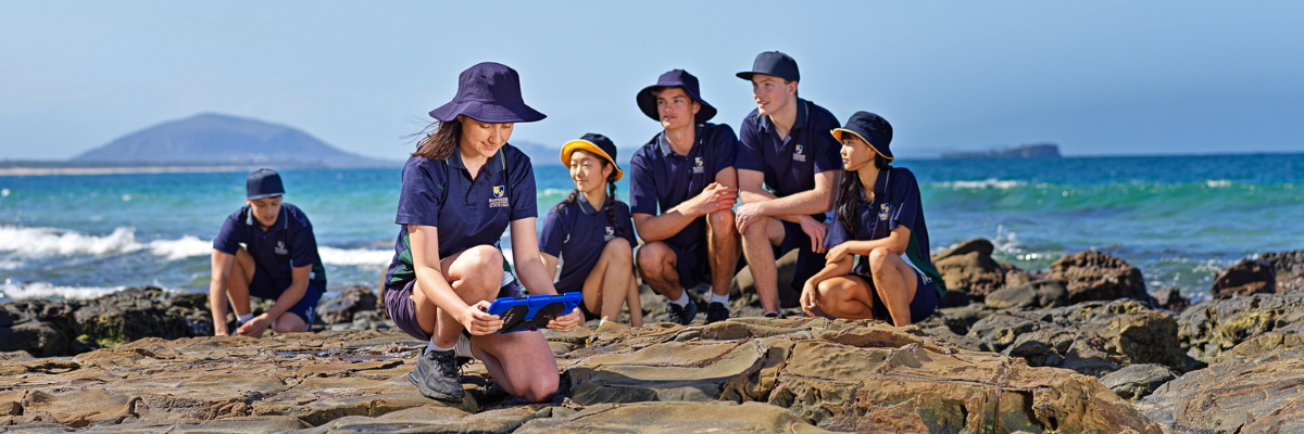 Students sitting on rock formations by the sea