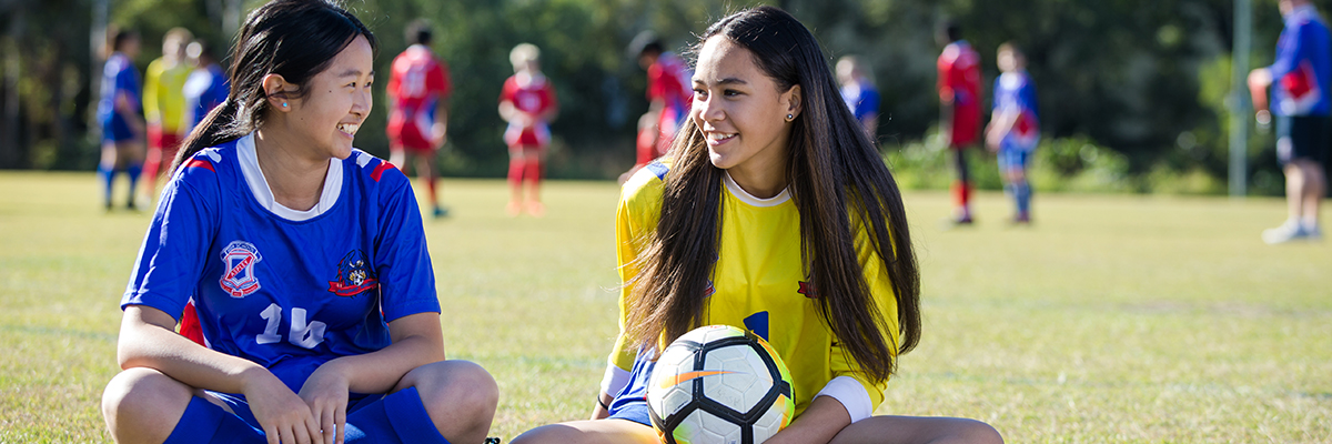 Students in conversation next to a game of soccer